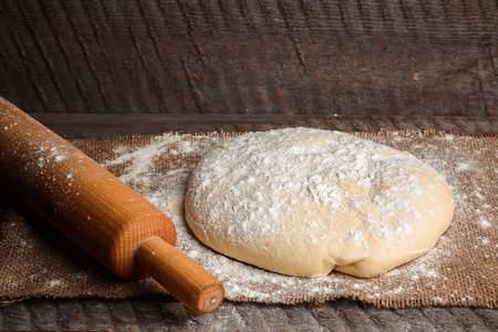 Ball of pizza dough and a rolling pin on a rustic wooden background with dusting of flourの写真素材
