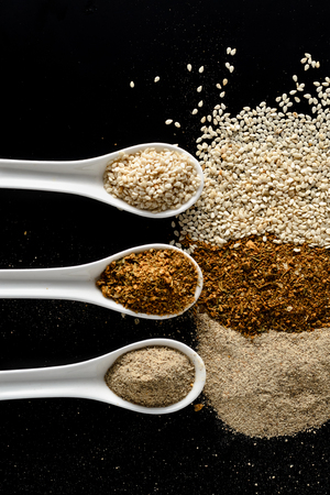 three porcelain spoons with spices on a black background isolated. Top viewの写真素材