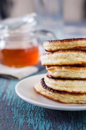 white plate full of pancakes on a wooden background and honey