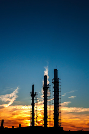 three pipes of a plant on a background of sunset and blue sky. Silhouette. Environmental problems, pollution of the environment. Vertical composition.の写真素材
