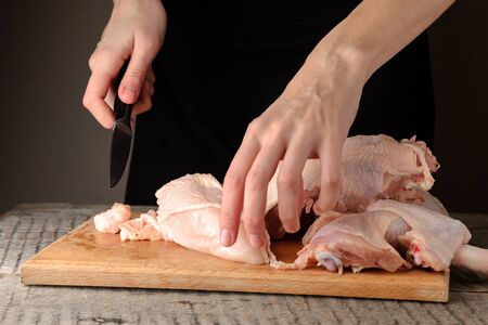 a man knives a raw chicken into pieces on a cutting board.の写真素材