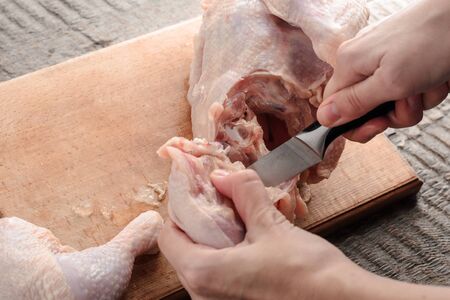 a girl knives a raw chicken into pieces on a cutting board.の写真素材