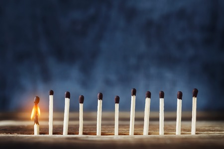row of matches, one is lit. One burning match to the left of the rest. Concept of the idea. Top place for textの写真素材