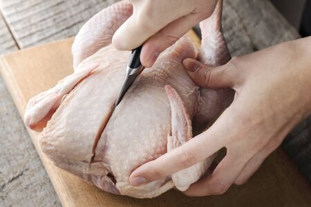 a girl knives a raw chicken into pieces on a cutting board.の写真素材