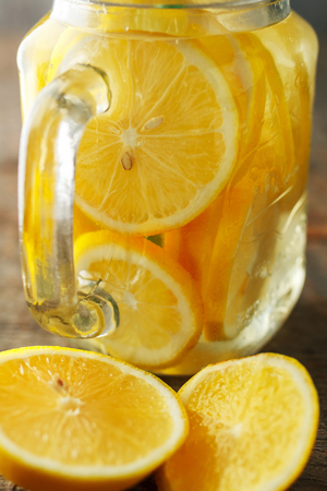 home made lemonade on a wooden background in contrasting lighting. Lemon slices in a jar filled with waterの写真素材