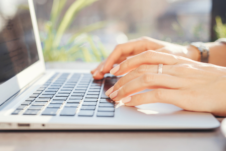 woman is sitting at a table in a cafe near the window and working behind a laptop. Organization of the workplaceの写真素材