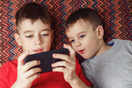 Two brothers lying playing a game in phoneの写真素材