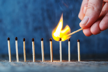 matches in a row on a wooden background, a hand with a burning match sets fire to another match.の写真素材