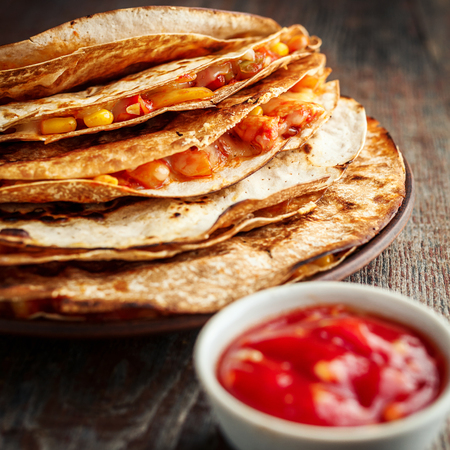 Mexican quesadilla, tortillas with chicken and trailing cheese and salsa sauce on a wooden backgroundの写真素材
