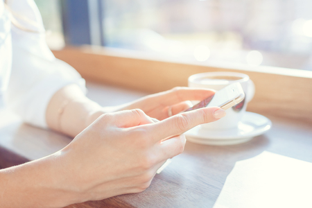 A young woman is holding a phone at a table in a cafe.の写真素材