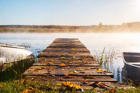 a long pier leading into the river, autumn leaves lie on the pier. Morning mist over the riverの写真素材