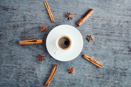a cup of espresso coffee on a saucer, cinnamon sticks and anise stars on a wooden background in a flat style.の写真素材