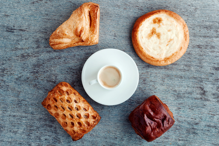 a cup of espresso on a saucer, buns and cakes on a wooden background. Top viewの写真素材