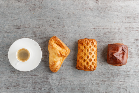 a cup of coffee and buns in a row on a gray wooden background.の写真素材
