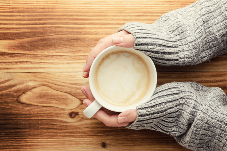the woman is holding a cup of coffee on a wooden tableの写真素材