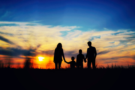 silhouettes of family members at sunset. Father, mother, and children hold hands on a sunset background.の写真素材
