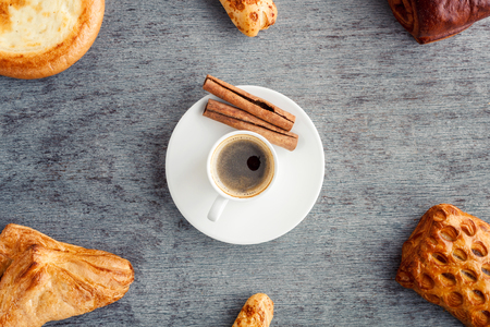Composition of a cup of coffee and cinnamon sticks with scattered around the buns on wooden background. A frame of cakes and croissants around a cup of coffeeの写真素材