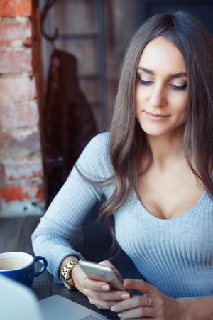 Young attractive woman working in a cafe and drinking coffee. the girl is reading a message on the phone.の写真素材