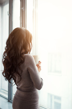 beautiful slender girl by the window with a cup of coffee in herの写真素材