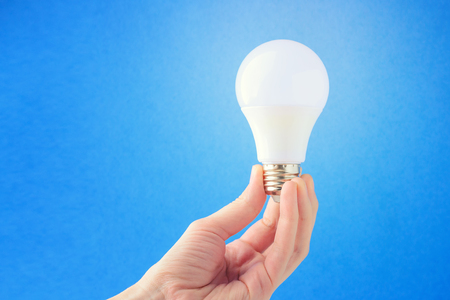 LED lamp in hand on a blue background. Concept of the idea. Copy spaceの写真素材