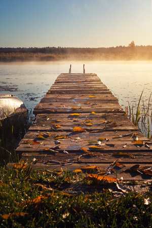 a bridge over a misty river leaving into the distance at dawn. Pier over the water in the morning light.の写真素材
