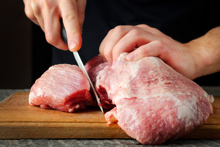 a man cuts a piece of pork meat on a cutting boardの写真素材