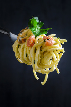 Pasta with seafood in a creamy sauce on a fork on a dark background. Close-up. Italian Cuisineの写真素材