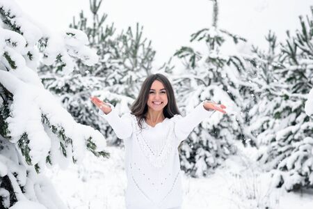 happy young woman in winter fir snowy forest throws up her hands snow.の写真素材