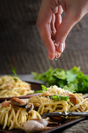 a woman sprinkles a Parmesan cheese paste of shrimp and mussels in a creamy sauce. Italian Cuisineの写真素材