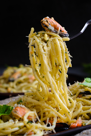 pasta with seafood in a creamy sauce wrapped on a fork rises from the plate. Italian cuisine, pasta with mussels and shrimps.の写真素材