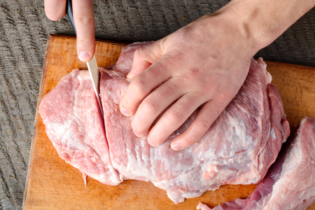 Man slices meat into pieces with a knife on a wooden cutting board on a dark backgroundの写真素材