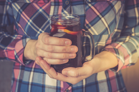 A young woman in a shirt is holding a mug of homemade mulled wine in her hands. Toned photoの写真素材