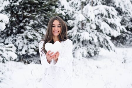 young woman in winter forest holding a heart from the snow and smiling. The girl gives her heartの写真素材