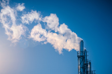 three chimneys smoking white smoke in a row against a blue sky in the sun. The concept of...