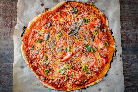 Homemade Italian pizza with salami, tomato and parmesan on a wooden background. Italian Cuisine. Top viewの写真素材