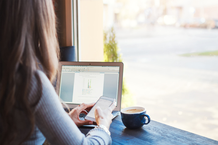 Attractive young business woman working on laptop in cafe. A modern workplace, a girl drinks coffee during a break between workの写真素材