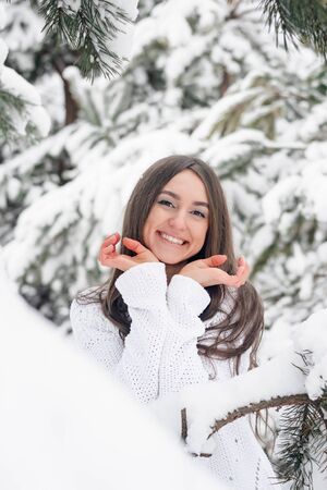 A beautiful young woman in a white jumper is happy in the winter fir forestの写真素材