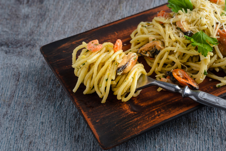 Pasta in a creamy sauce with seafood, shrimps and mussels, wrapped on a fork in a clay plate on a dark wooden backgroundの写真素材