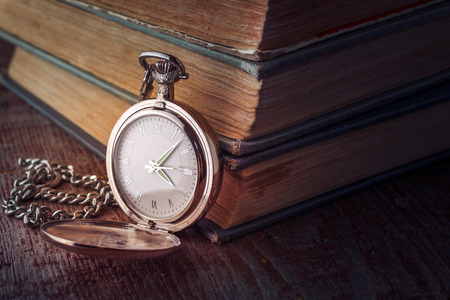dial Vintage pocket watch on a chain and old books on a wooden background. Tinted picture in low keyの写真素材