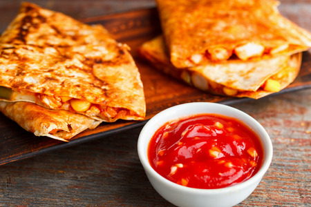 two pieces of quesadilla on a plate and sauce of salsa on a wooden background. National Mexican cuisine, fast food.の写真素材