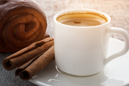 A cup of fragrant coffee on a white plate, cake and cinnamon sticks on a wooden background.の写真素材