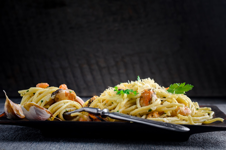 Italian pasta in a creamy sauce with seafood, shrimps and mussels on a plate on a dark wooden backgroundの写真素材