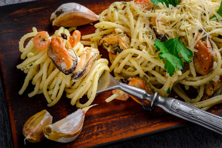 Italian pasta in a creamy sauce with seafood, shrimps and mussels on a plate on a dark wooden backgroundの写真素材