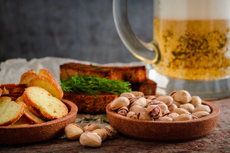 Beer in a glass, pistachios, rye croutons with dill and crackers on a wooden tableの写真素材