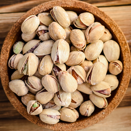 a bunch of pistachios nuts in a brown cork plate on a wooden background. Top viewの写真素材