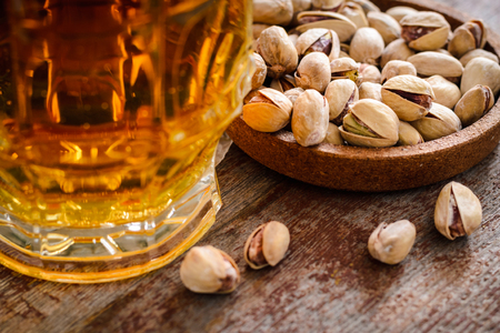 a glass of light beer and a handful of pistachios on a wooden table. Close-upの写真素材