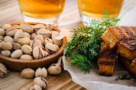 two glasses of beer, salted pistachios and toasts of bread with dill on a wooden table in the backlightの写真素材