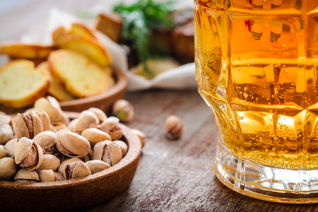 A beer mug and salted pistachios on a wooden table in the backlightの写真素材