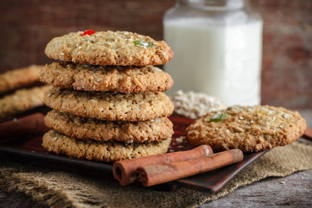 Homemade oatmeal cookies, stacked, cinnamon sticks and a glass of milk on a wooden backgroundの写真素材
