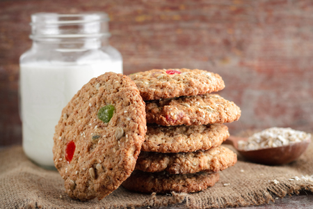 Homemade oatmeal cookies with dried fruits and sunflower seeds, stacked, and a mug of milk on a wooden backgroundの写真素材